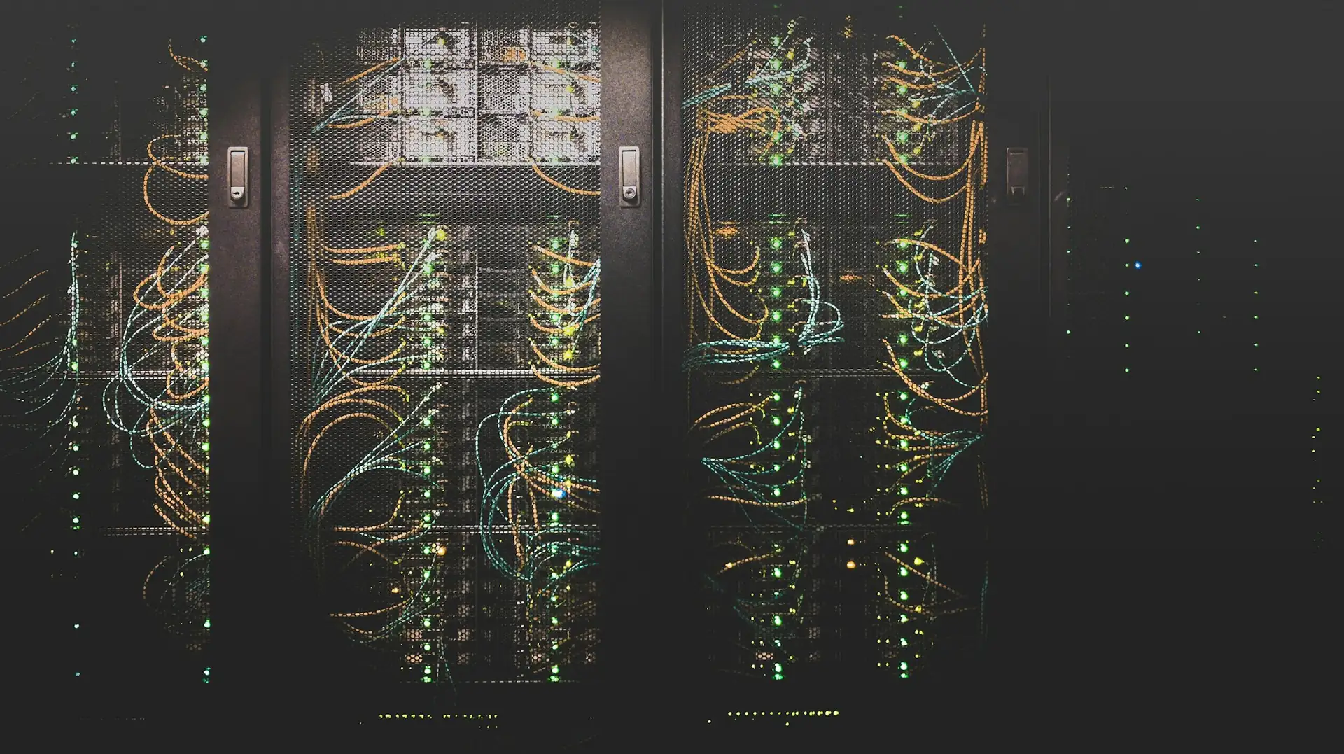 Baies de serveurs à portes grillagées, câblées en orange et en bleu, voyants verts allumés